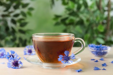 Photo of Glass cup of tea and cornflowers on wooden table