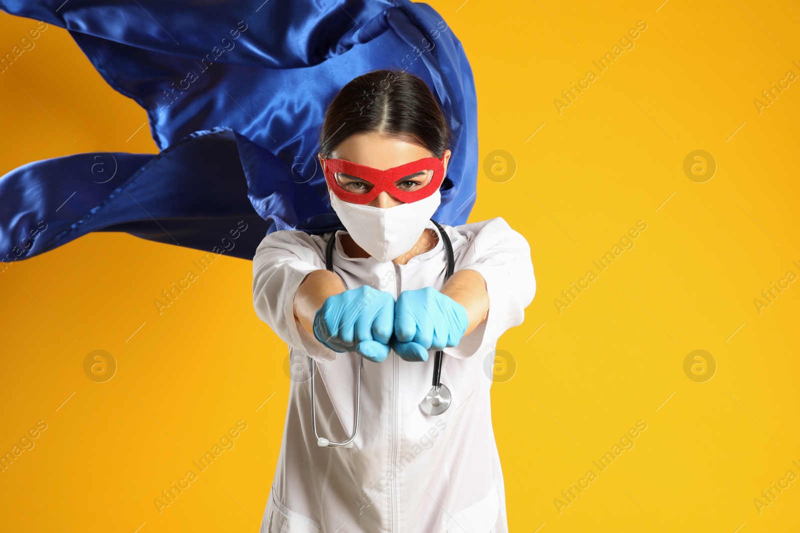 Photo of Doctor dressed as superhero posing on yellow background. Concept of medical workers fighting with COVID-19