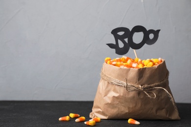 Photo of Paper bag with tasty candy corns on table against gray background. Space for text