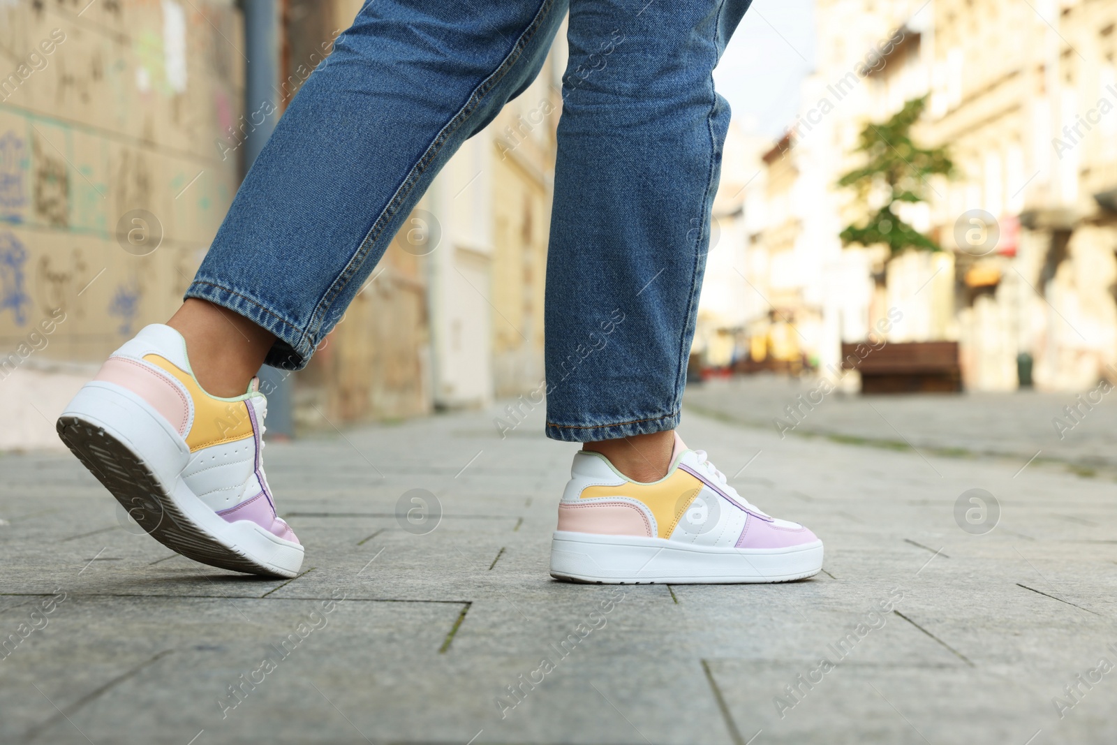 Photo of Woman in stylish sneakers walking on city street, closeup