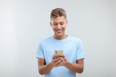 Photo of Happy young man sending message via smartphone on light grey background