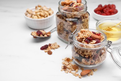 Jars of tasty granola with nuts and dry fruits on white marble table. Space for text