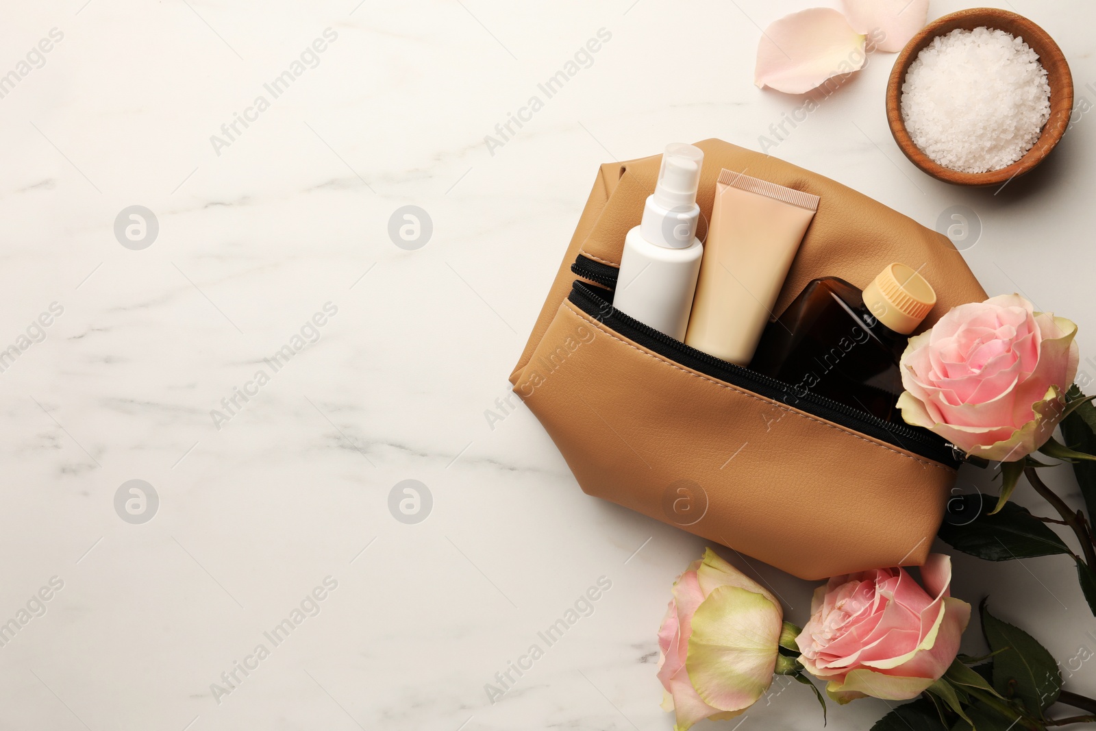 Photo of Preparation for spa. Compact toiletry bag, flowers and different cosmetic products on white marble table, flat lay with space for text