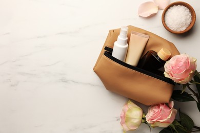 Photo of Preparation for spa. Compact toiletry bag, flowers and different cosmetic products on white marble table, flat lay with space for text