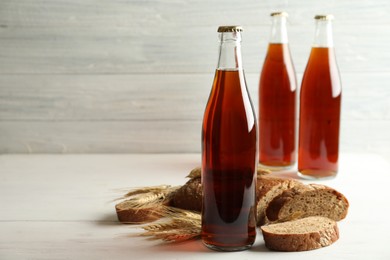 Photo of Bottle of delicious fresh kvass, spikelets and bread on white wooden table. Space for text