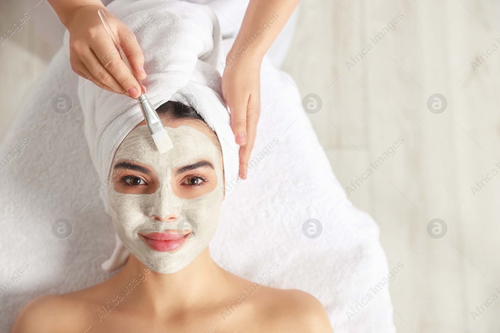 Photo of Cosmetologist applying mask on woman's face in spa salon, top view. Space for text