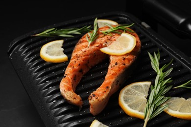 Photo of Cooking salmon. Grill with tasty fish steak, lemon and rosemary on grey table, closeup