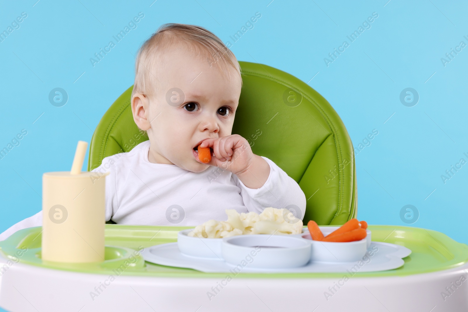 Photo of Cute little baby eating healthy food in high chair on light blue background