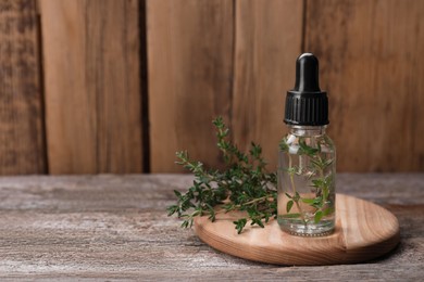 Photo of Bottle of thyme essential oil and fresh plant on wooden table, space for text