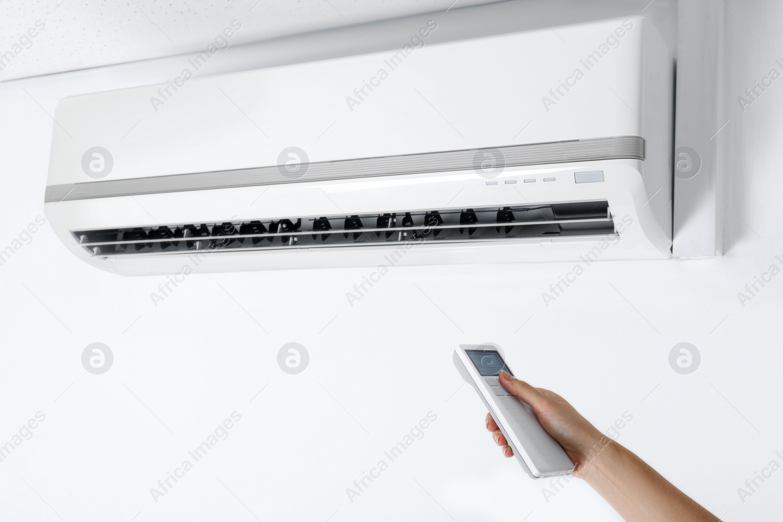 Photo of Woman operating air conditioner with remote control indoors, closeup