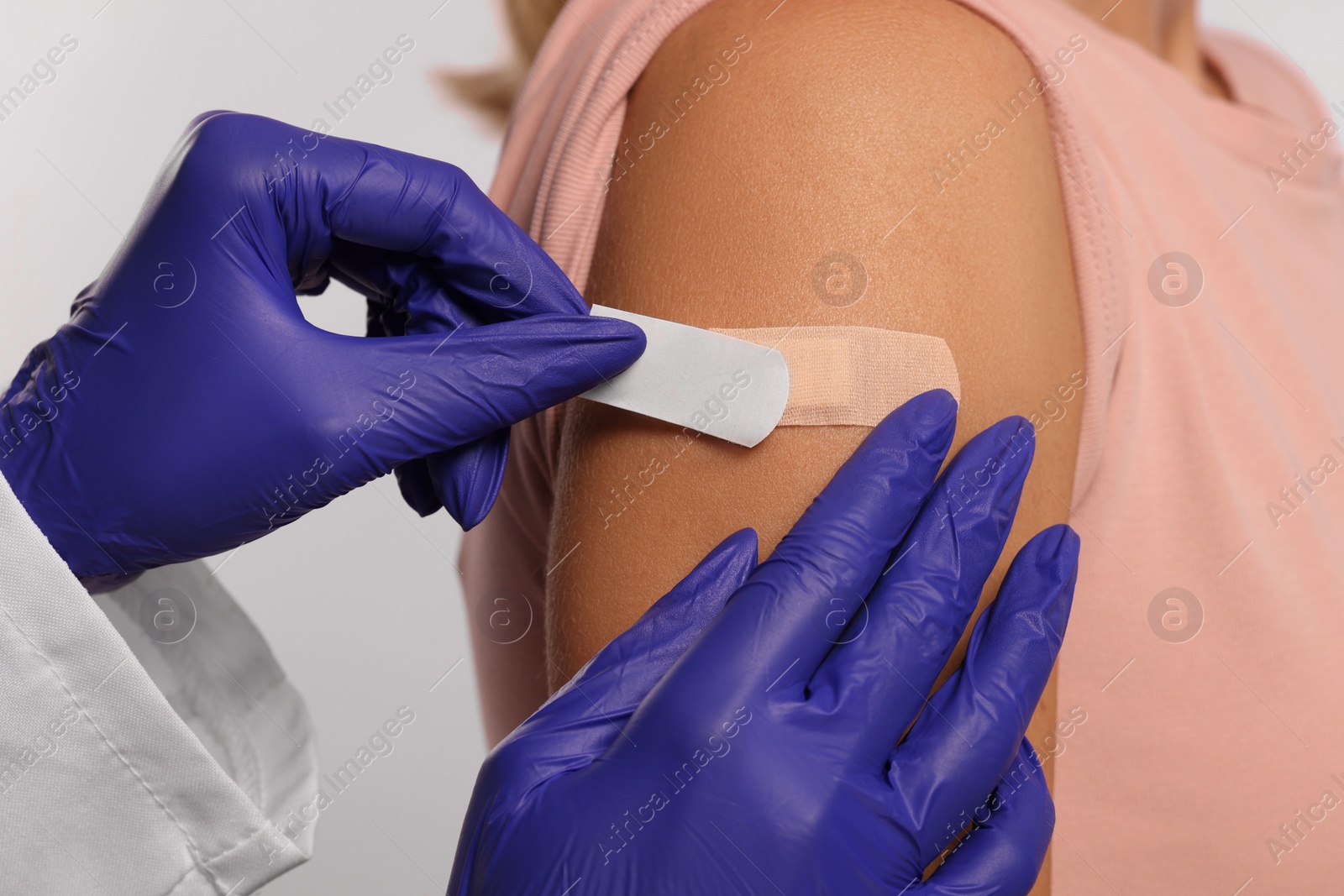 Photo of Nurse sticking adhesive bandage on woman's arm after vaccination on light background, closeup