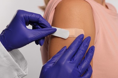 Photo of Nurse sticking adhesive bandage on woman's arm after vaccination on light background, closeup