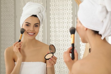 Photo of Beautiful young woman applying face powder with brush in front of mirror at home