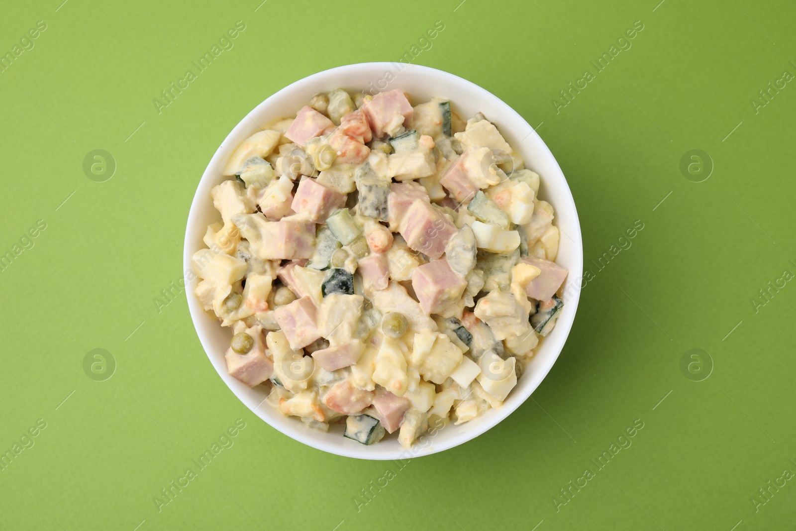 Photo of Tasty Olivier salad with boiled sausage in bowl on green table, top view