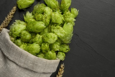 Photo of Sack with fresh green hops and spikes on black table, flat lay