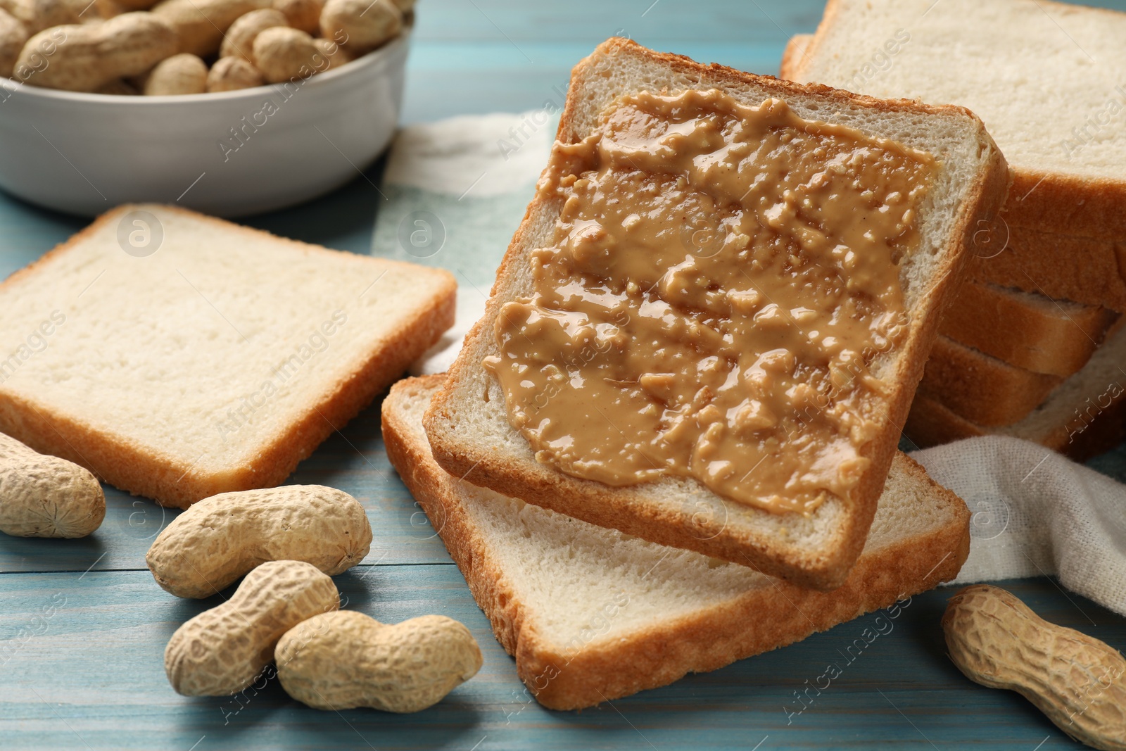 Photo of Delicious toasts with peanut butter and nuts on light blue wooden table, closeup