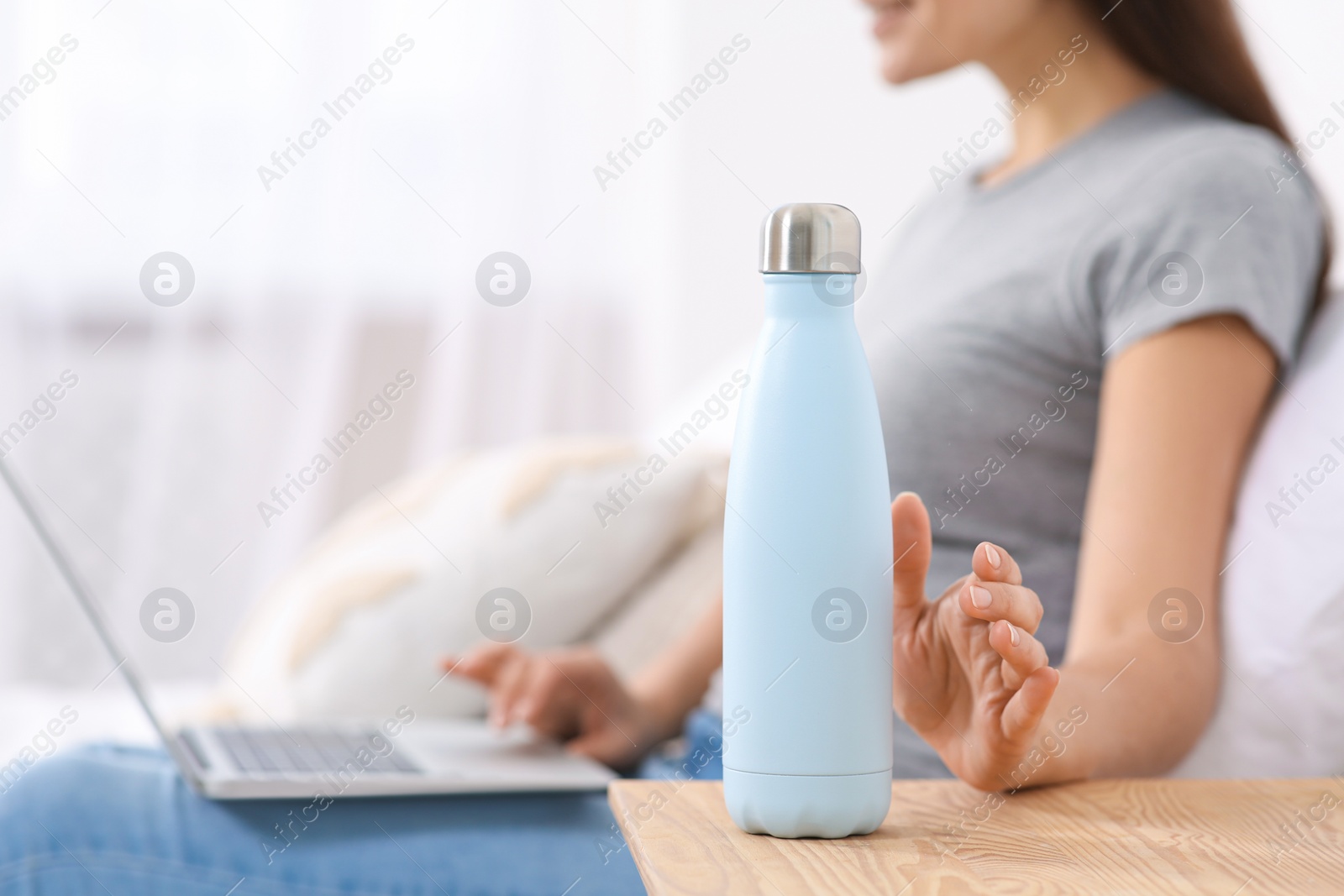 Photo of Woman with laptop taking thermo bottle in bedroom, closeup. Space for text