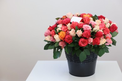 Photo of Bouquet of beautiful roses with blank card on white table against light background, space for text