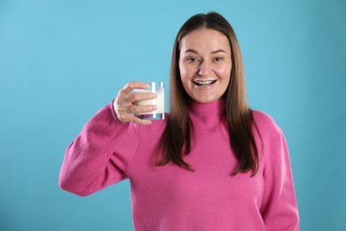 Happy woman with milk mustache holding glass of drink on light blue background