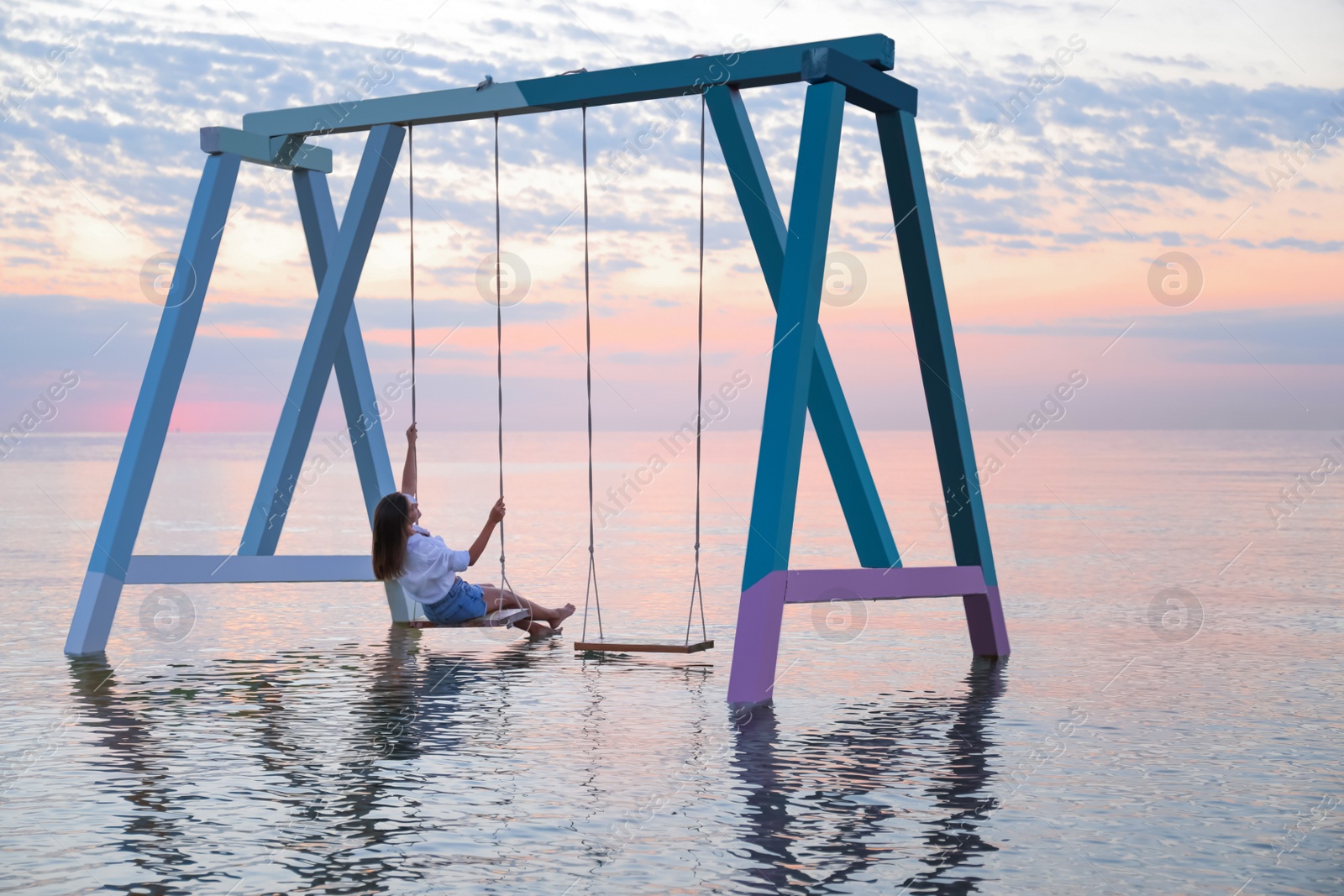 Photo of Young woman enjoying sunrise on swing over water