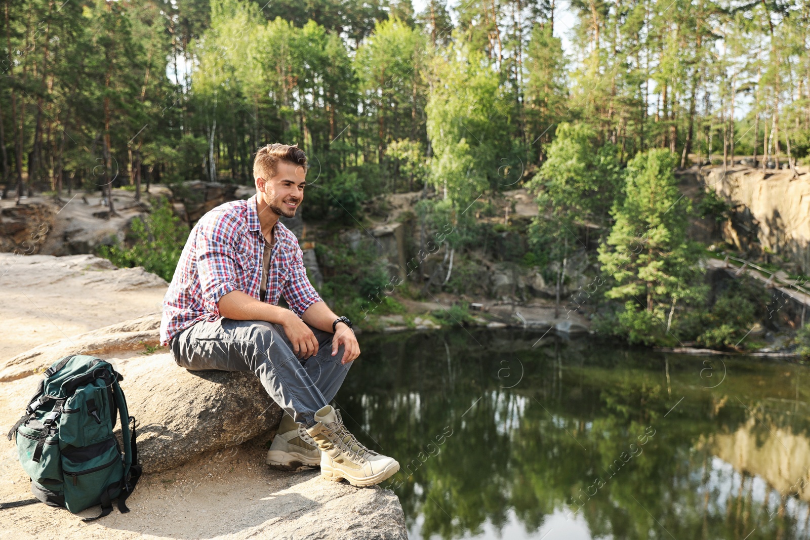 Photo of Young man on rock near lake and forest. Camping season