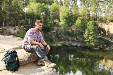 Young man on rock near lake and forest. Camping season