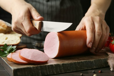 Photo of Woman cutting tasty boiled sausage at dark table, closeup