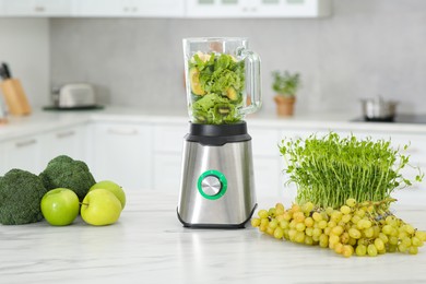 Photo of Blender with ingredients for smoothie and products on white marble table in kitchen