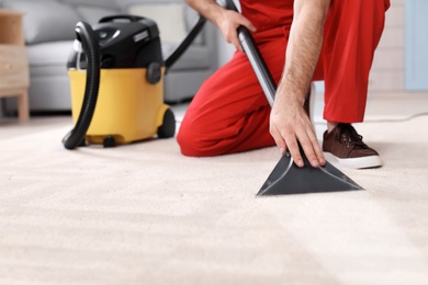 Male worker cleaning carpet with vacuum in living room