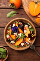 Photo of Delicious persimmon salad with cheese and pomegranate served on wooden table, flat lay