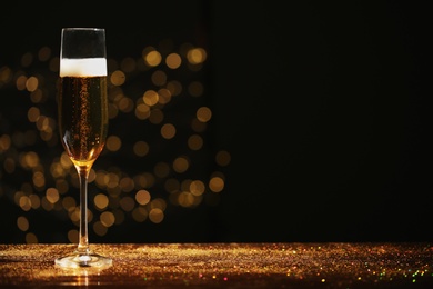 Glass of champagne and golden glitter on table against blurred background. Space for text
