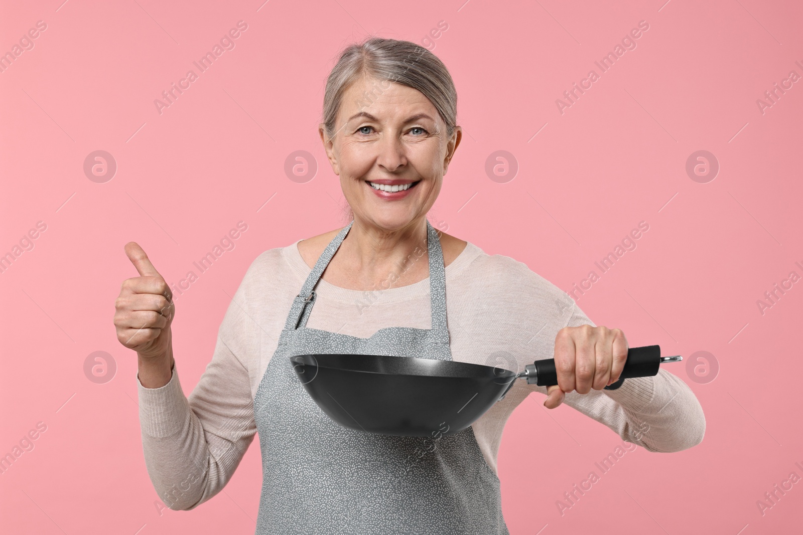 Photo of Happy housewife with frying pan showing thumbs up on pink background