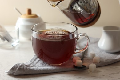 Photo of Pouring warm tea into cup on white wooden table, closeup