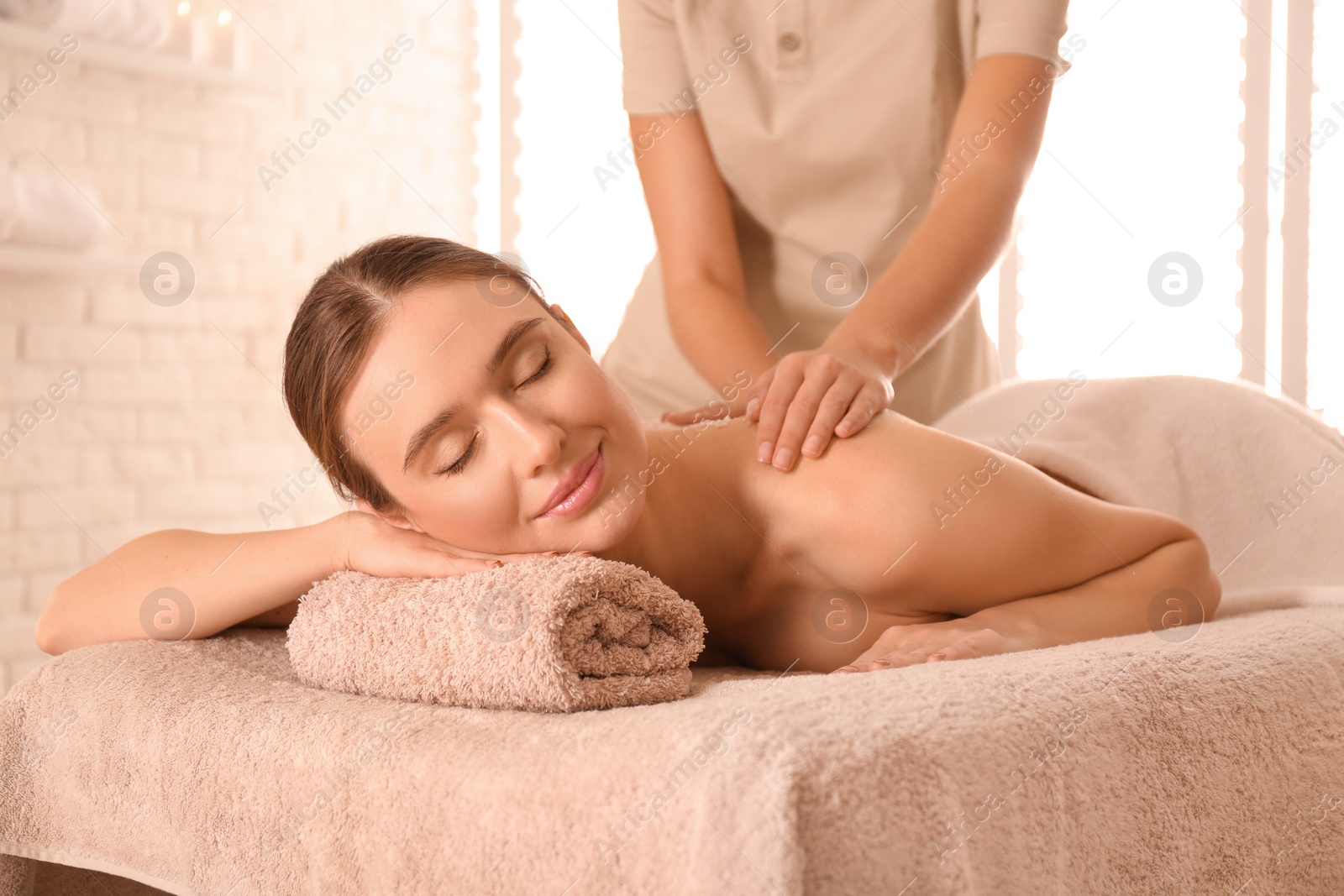 Photo of Young woman having body scrubbing procedure with sea salt in spa salon