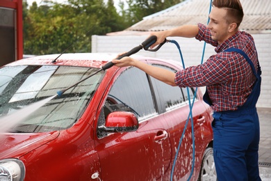 Male worker cleaning vehicle with high pressure water jet at car wash