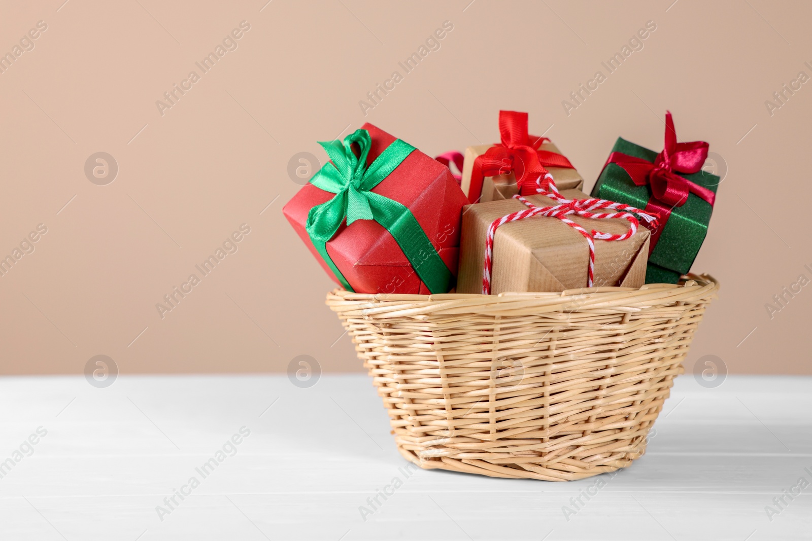 Photo of Wicker basket full of gift boxes on white wooden table against beige background. Space for text