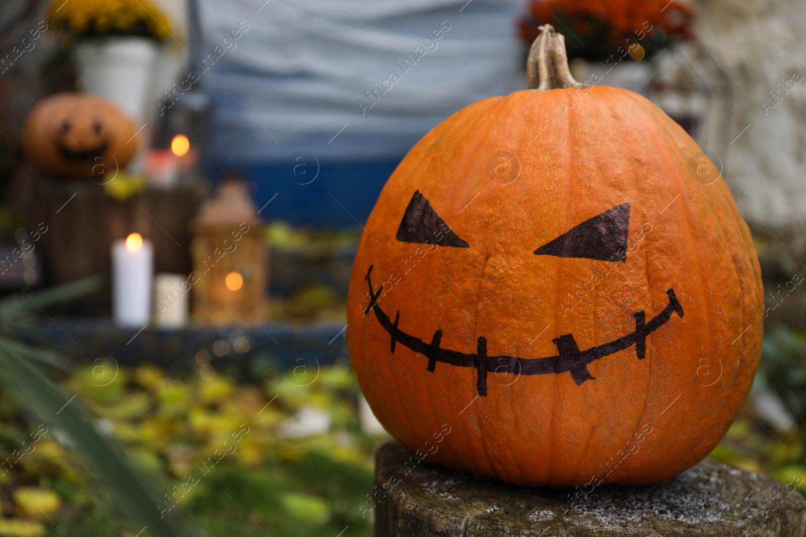 Photo of Jack o lantern with drawn scary face on wooden stump near house entrance decorated for traditional Halloween celebration