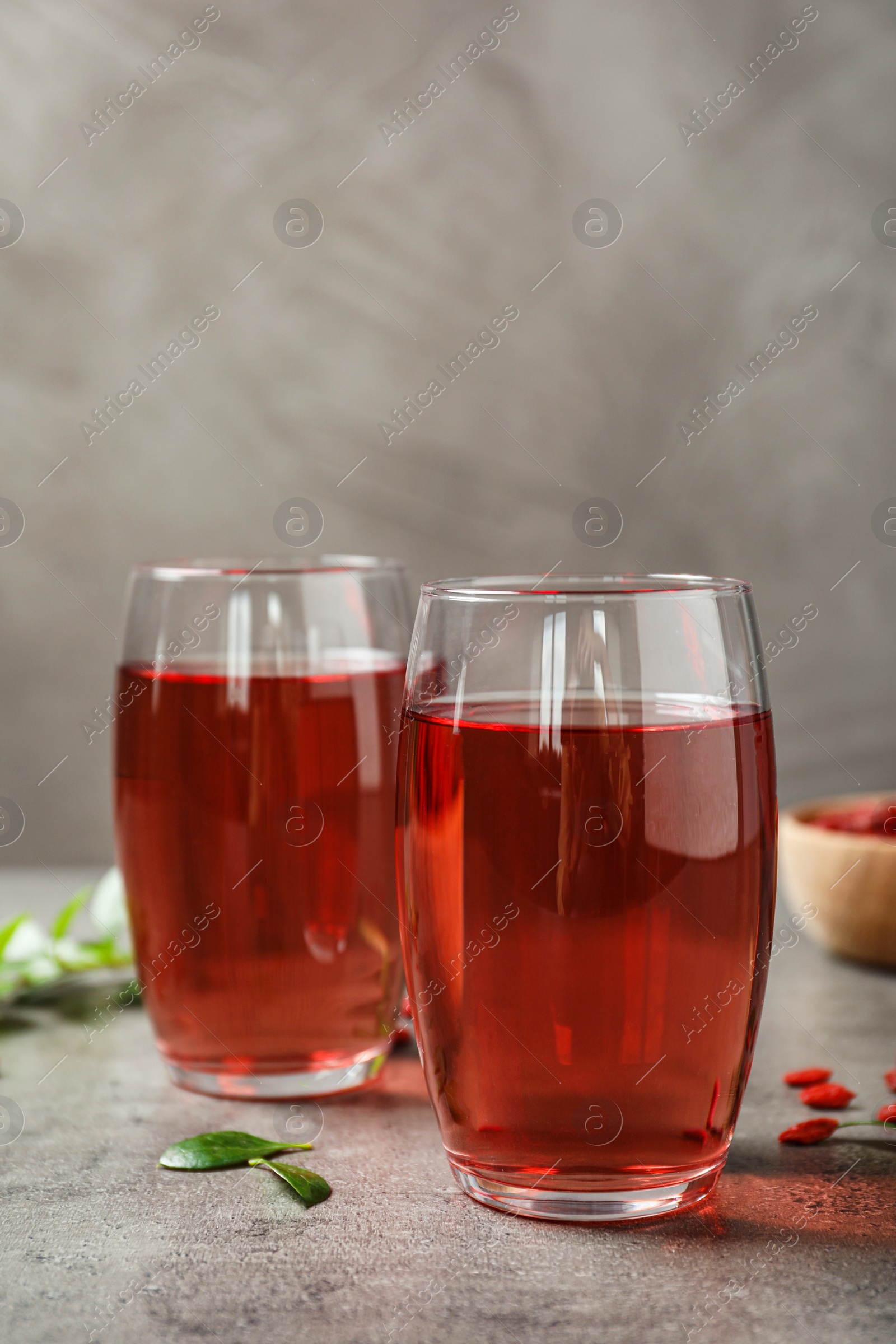 Photo of Glasses of healthy goji juice on grey table. Space for text