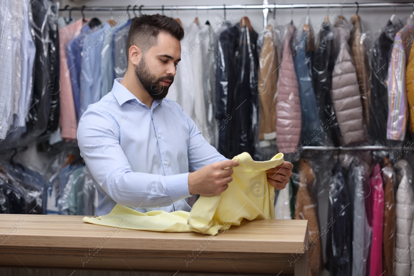 Photo of Dry-cleaning service. Worker holding t-shirt at counter indoors, space for text