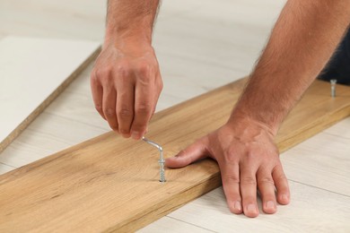 Photo of Man with hex key assembling furniture on floor, closeup