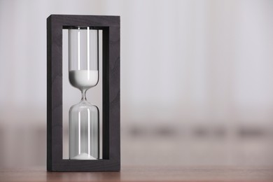 Photo of Hourglass with flowing sand on table against light background. Space for text