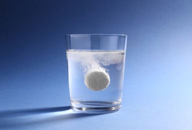 Effervescent pill dissolving in glass of water on blue background