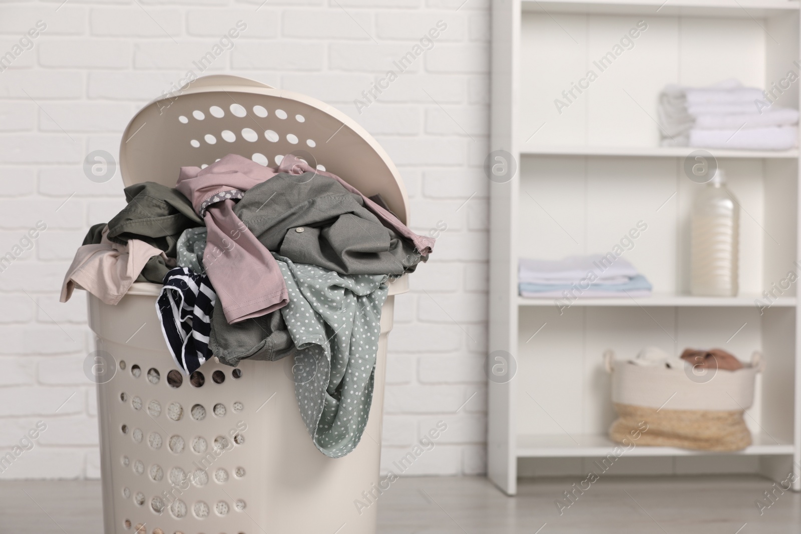 Photo of Plastic laundry basket overfilled with clothes indoors. Space for text