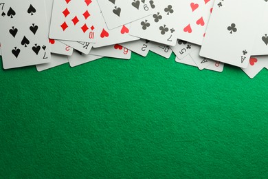 Photo of Scattered playing cards on green table, top view. Space for text