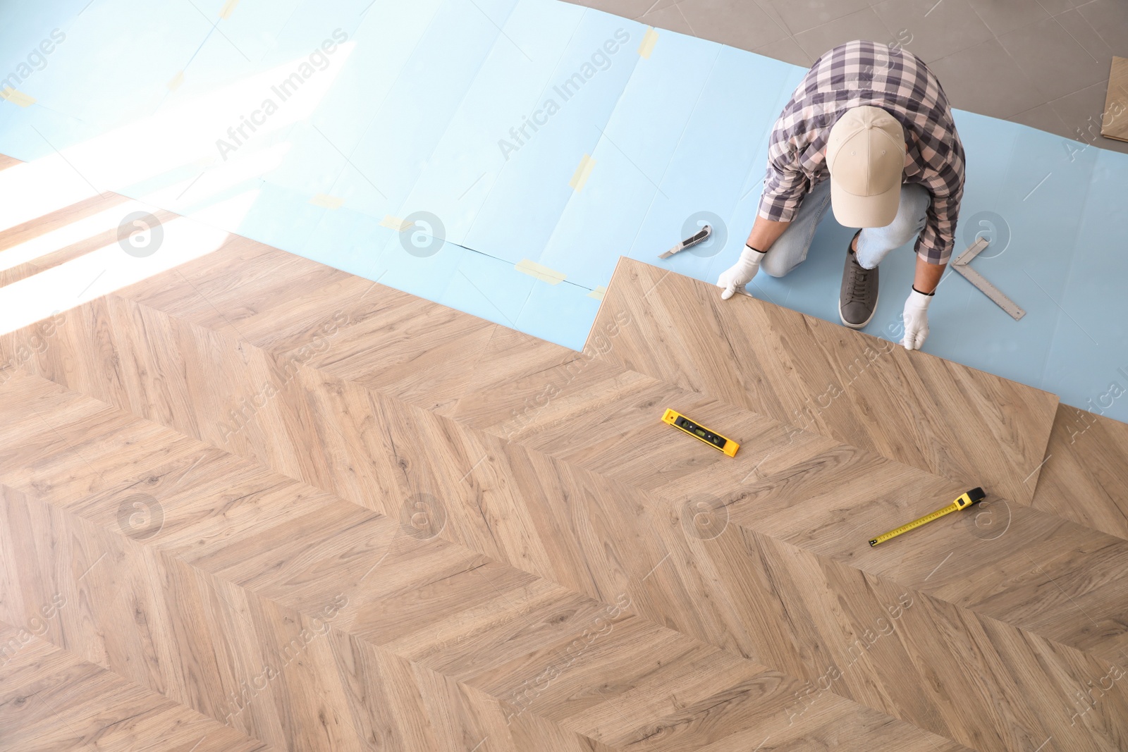 Photo of Worker installing laminated wooden floor indoors, above view