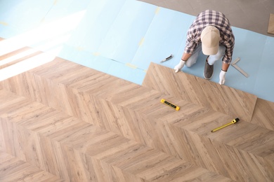 Photo of Worker installing laminated wooden floor indoors, above view