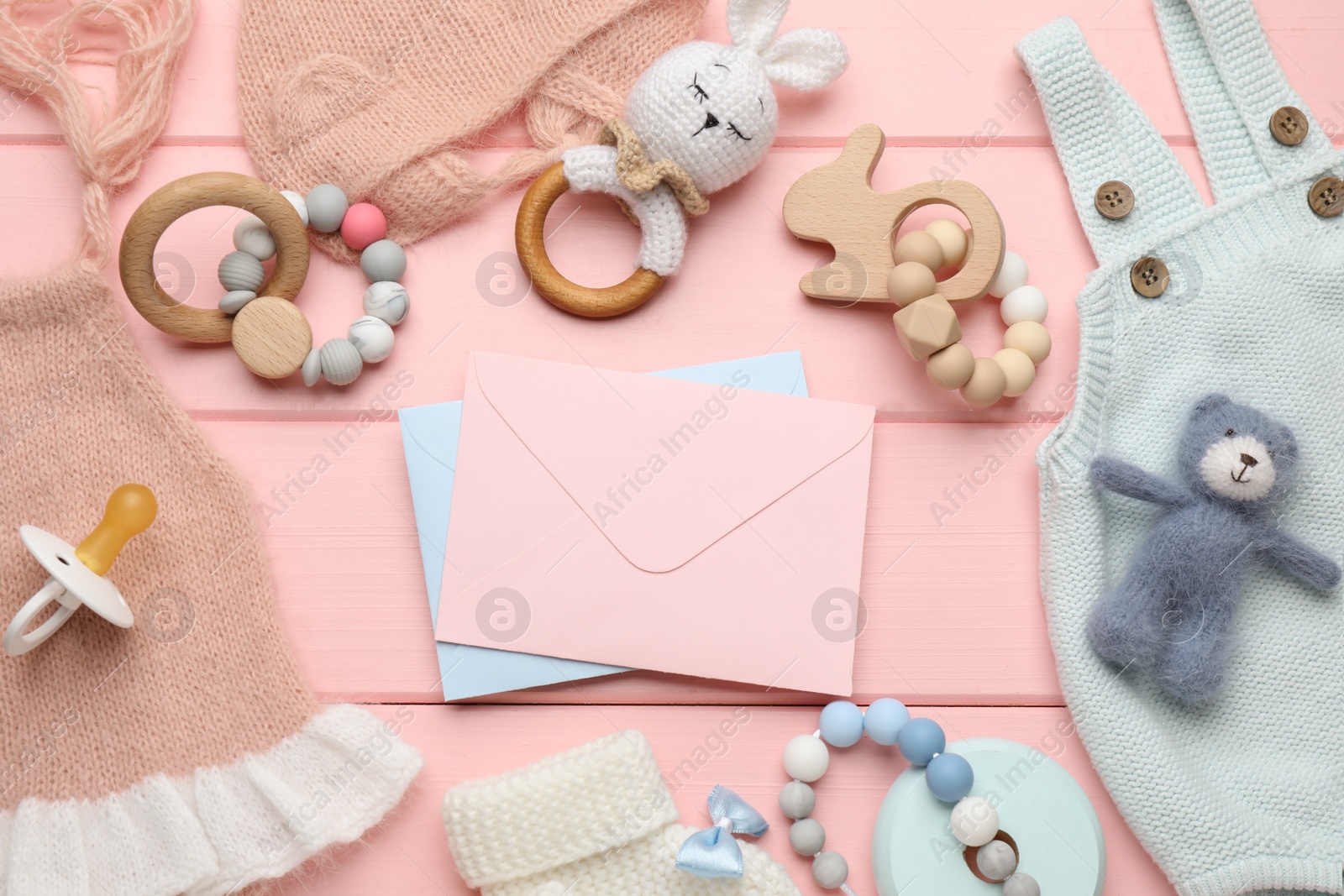 Photo of Baby shower party. Envelopes surrounded by stuff for child on pink wooden background, flat lay