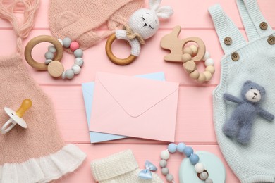 Baby shower party. Envelopes surrounded by stuff for child on pink wooden background, flat lay