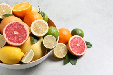 Different fresh citrus fruits and leaves in bowl on light table, closeup