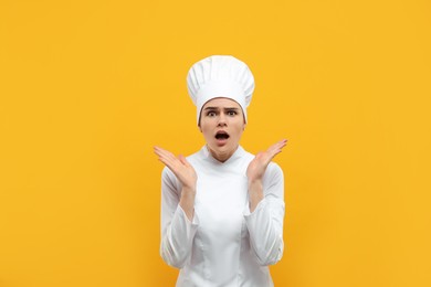 Emotional female chef wearing uniform and cap on orange background